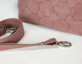 Pink leather dog leash with metal clip on a white surface, with a pink textured bag in the background.