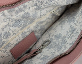 Pink leather dog leash with metal clip on a white surface, with a pink textured bag in the background.