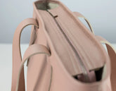 Close-up of a blush pink pebbled leather tote bag showing the interior zippered compartment and side handles.
