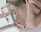 A close-up of a dusty pink pebbled leather tote bag shown open, displaying its interior lining, zipper pocket, and strap attachment on a white background.