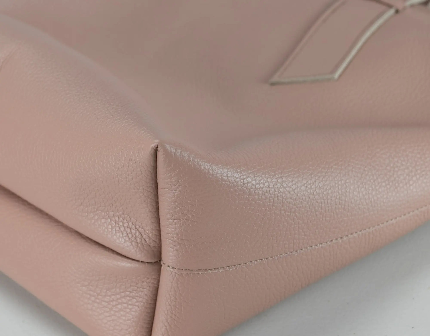 Close-up of a blush pink pebbled leather handbag corner showing the texture and stitching detail.