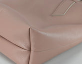 Close-up of a blush pink pebbled leather handbag corner showing the texture and stitching detail.