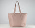 A light pink leather tote bag with dual shoulder straps, displayed on a white surface against a neutral light gray background.