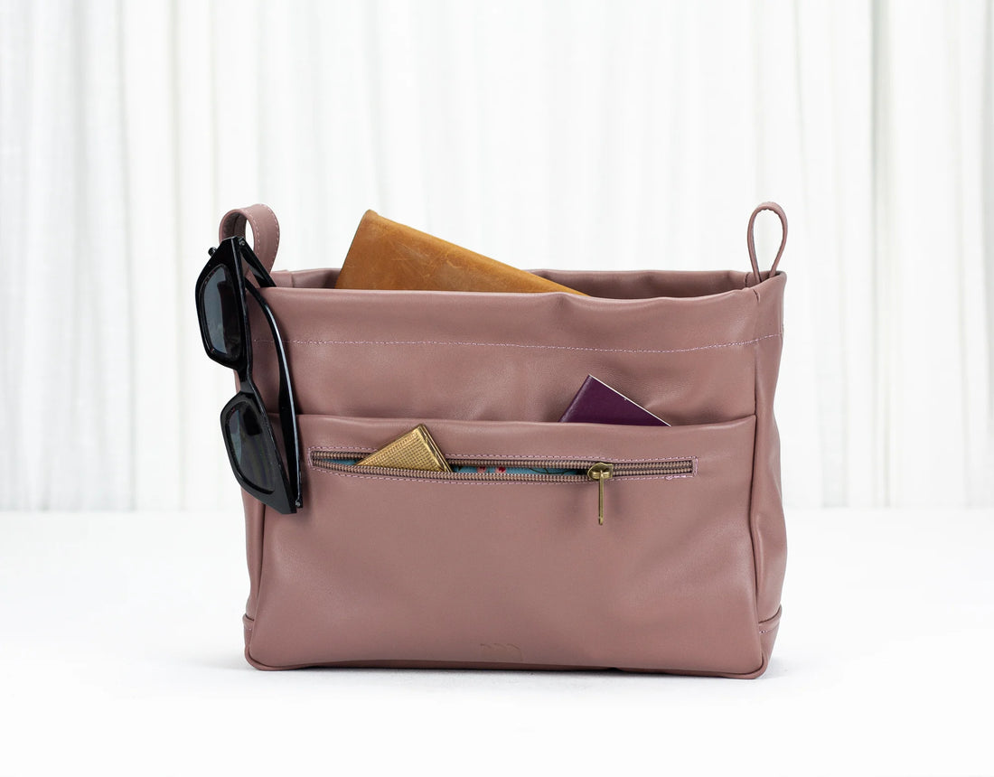 Pink bag with sunglasses and a phone inside on a white background