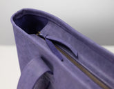 Close-up detail of a purple leather tote bag showing the interior lining, zipper track, and strap attachment.