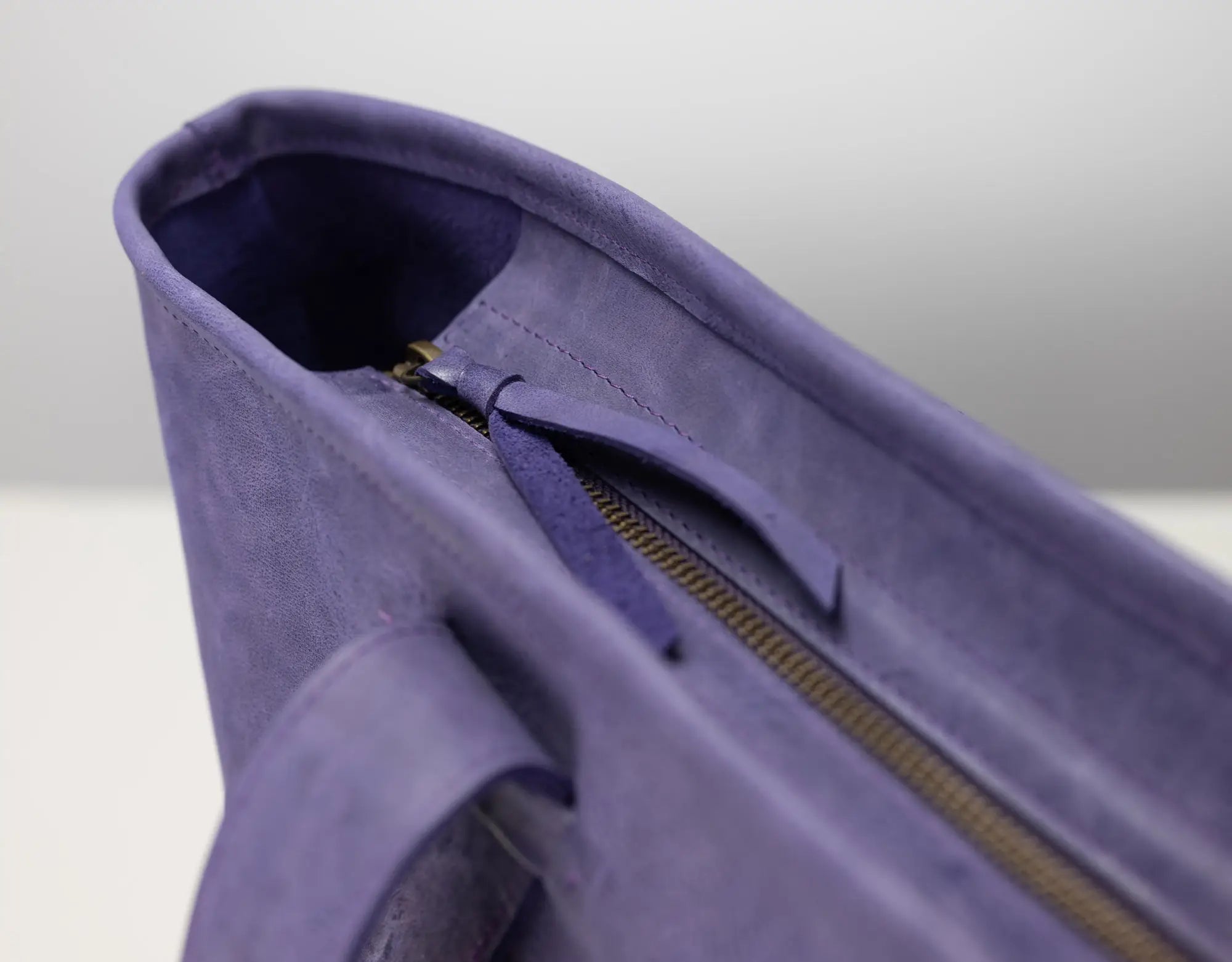 Close-up detail of a purple leather tote bag showing the interior lining, zipper track, and strap attachment.