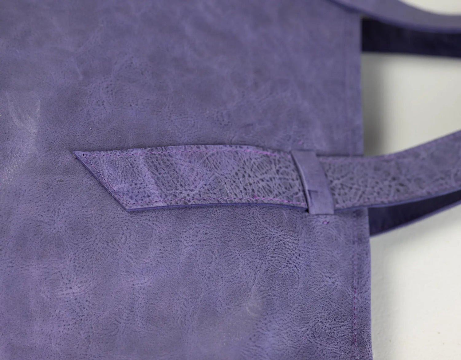 Close-up of a purple leather tote bag showing a front pocket with a matching strap and a textured, distressed finish.
