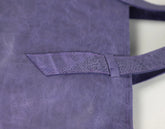 Close-up of a purple leather tote bag showing a front pocket with a matching strap and a textured, distressed finish.