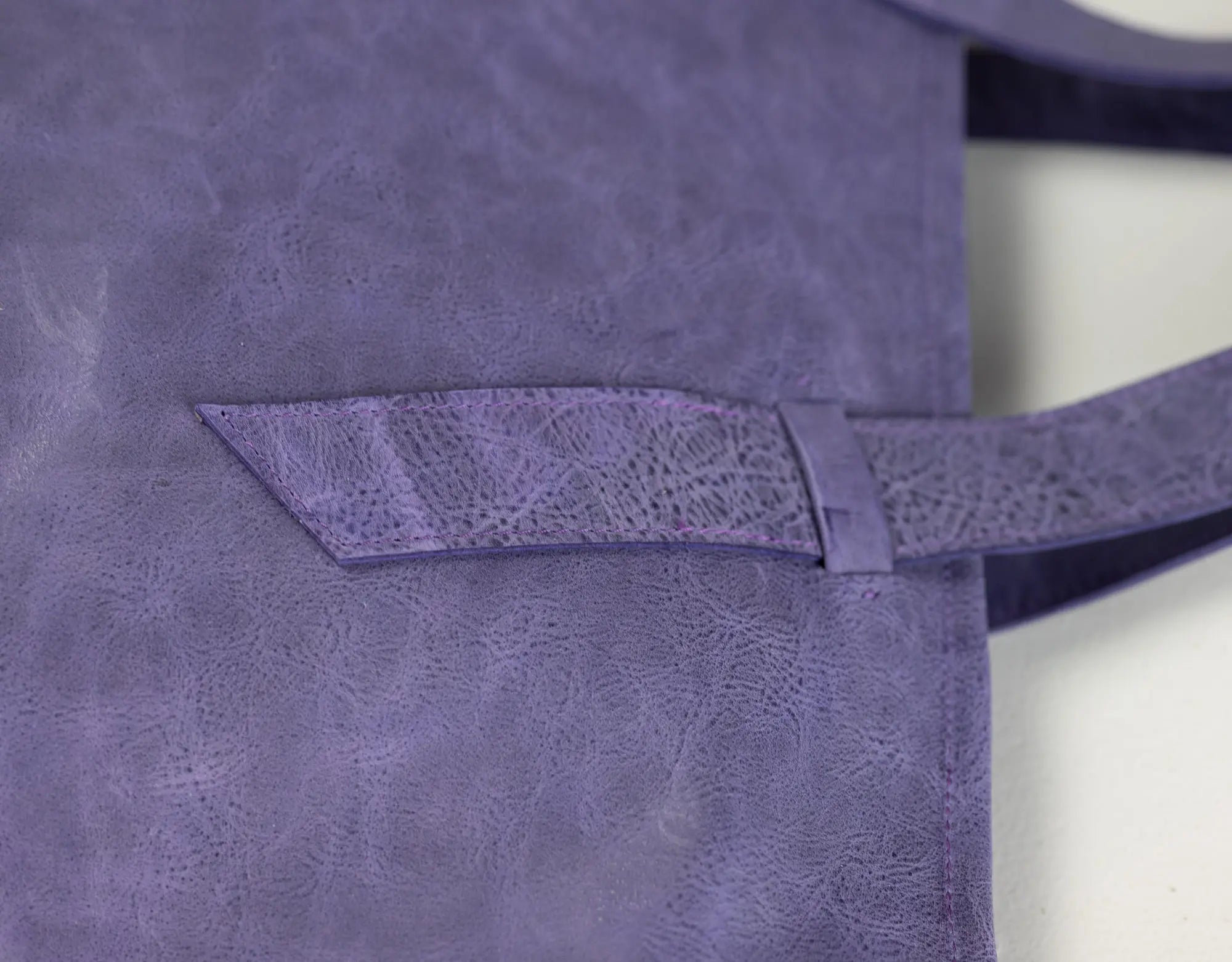 Close-up of a purple leather tote bag showing a front pocket with a matching strap and a textured, distressed finish.