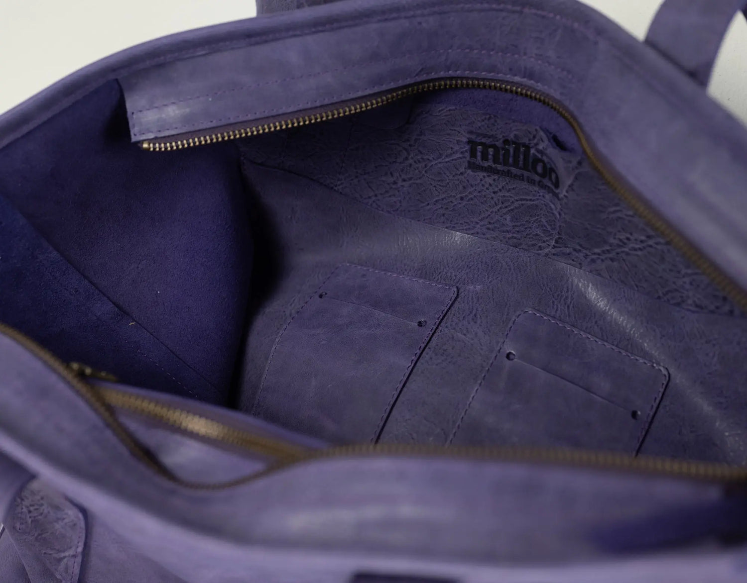 Close-up of the interior of a purple leather tote bag, showing a zippered compartment, interior pockets, and a black &