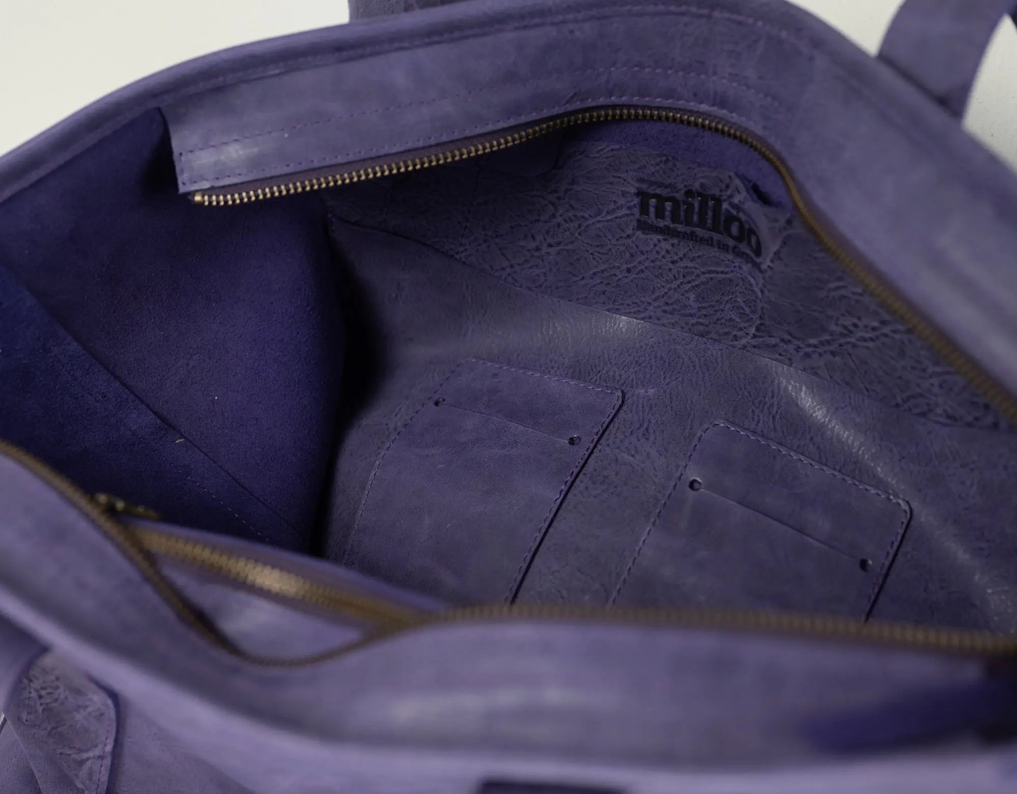 Close-up of the interior of a purple leather tote bag, showing a zippered compartment, interior pockets, and a black &