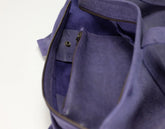 Close-up of the interior of a purple leather bag, showing a zippered pocket with a brass snap closure and a gold-toned zipper.