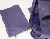 A purple leather zippered pouch shown next to an open matching purple bag, highlighting the interior and hardware on a plain white background.