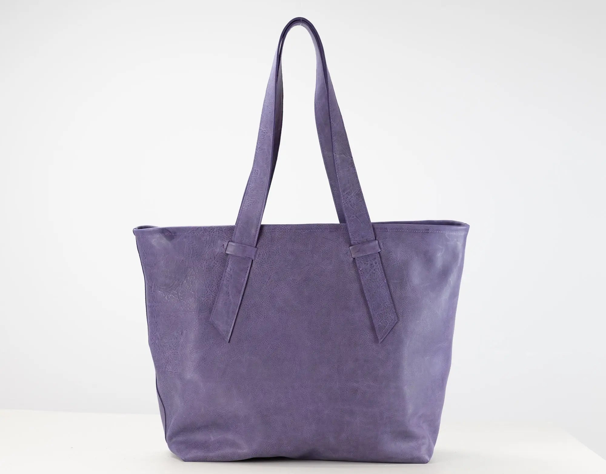 A purple leather tote bag with two shoulder straps, displayed against a clean white studio background.