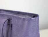 Close-up detail of a lavender purple textured leather tote bag corner, showing the stitched rim and part of the dark zipper pull.