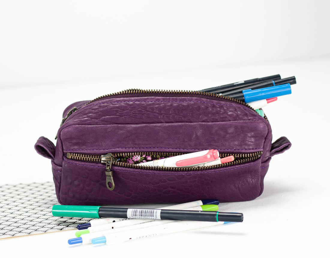 Purple pencil case with stationery items on a white background