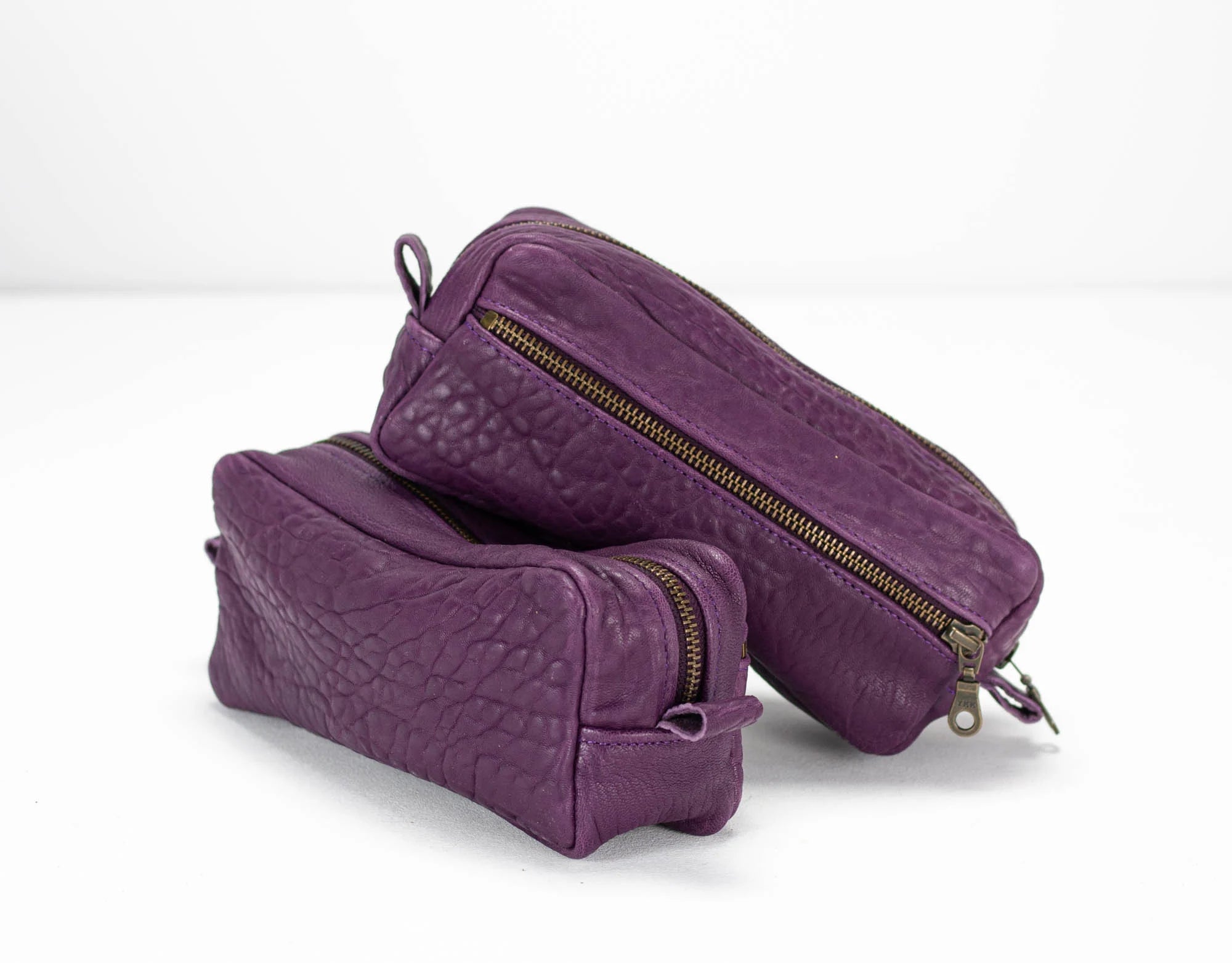 Two purple toiletry bags with gold zippers on a white background