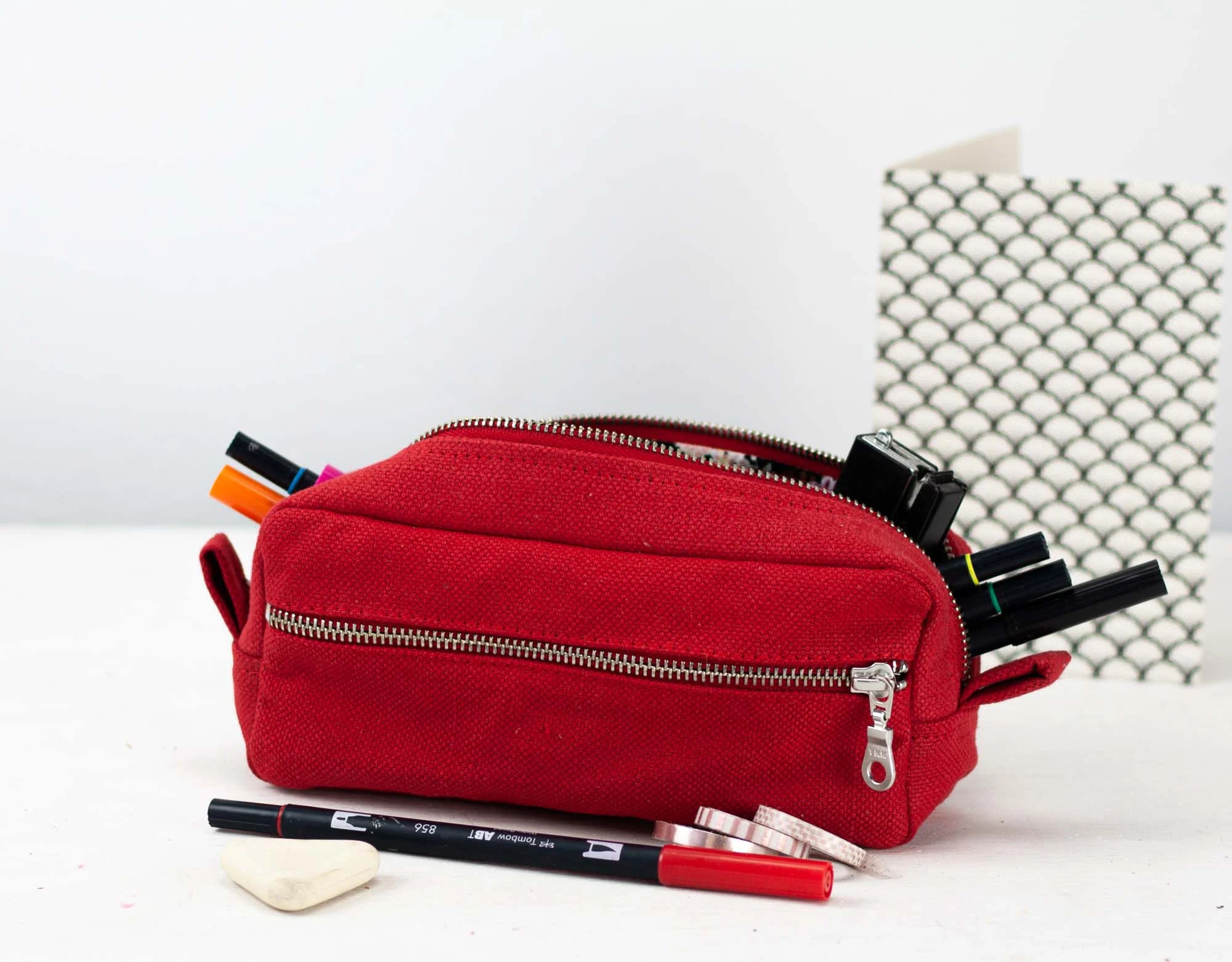 Red cotton pencil case with stationery items on a white background