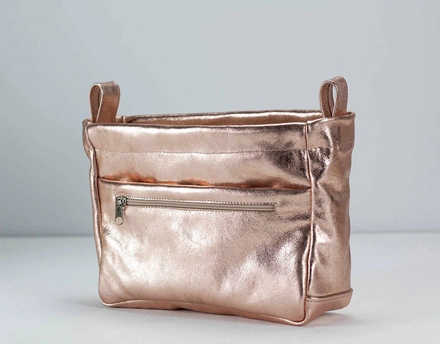 Rose gold metallic handbag with a zipper on a light gray background