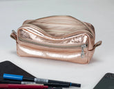 Rose gold metallic pouch with pens and a phone on a white background