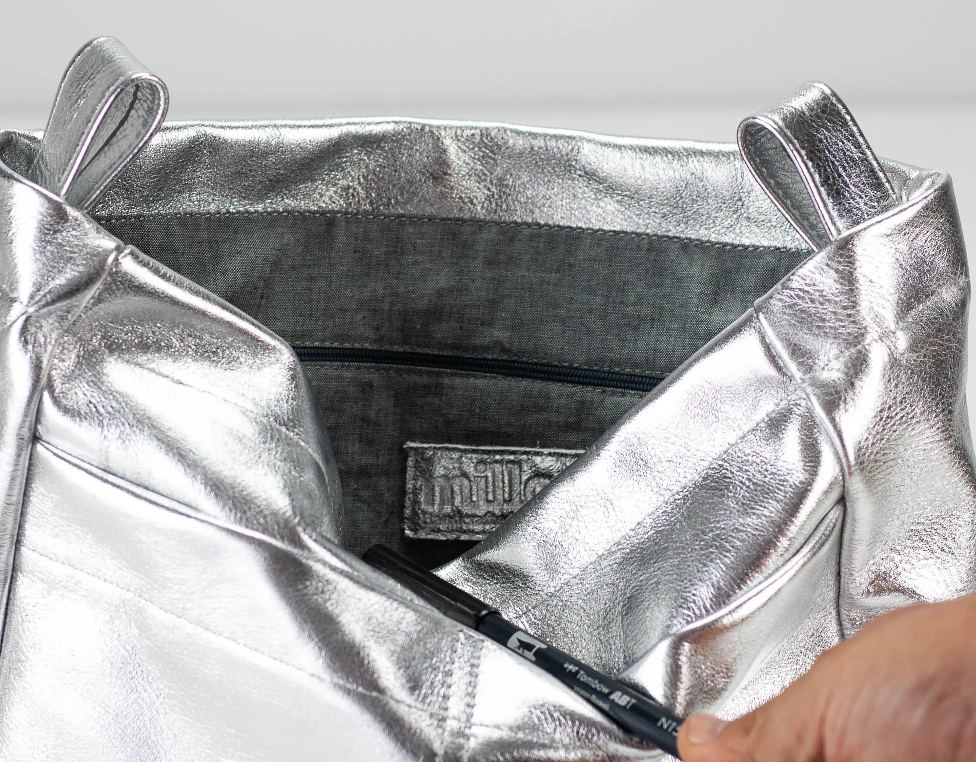 Silver metallic bag with a visible brand logo on a light gray background