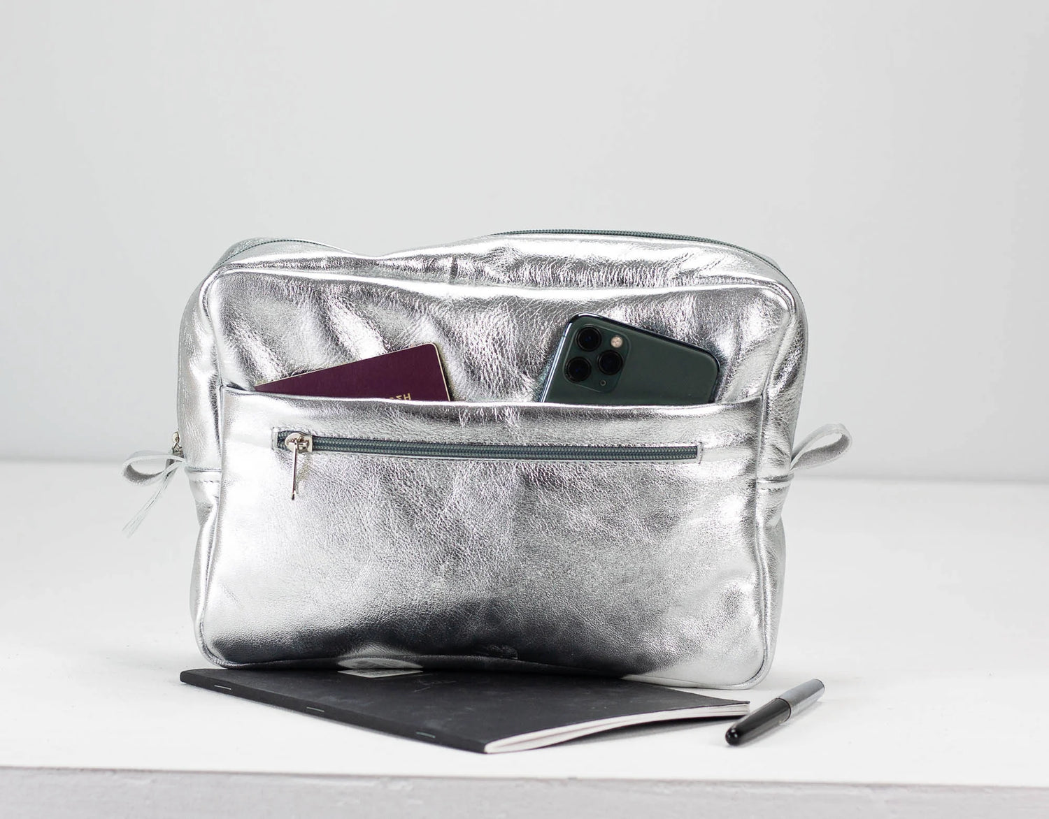 Silver pouch with phone, passport, and tablet on a white background