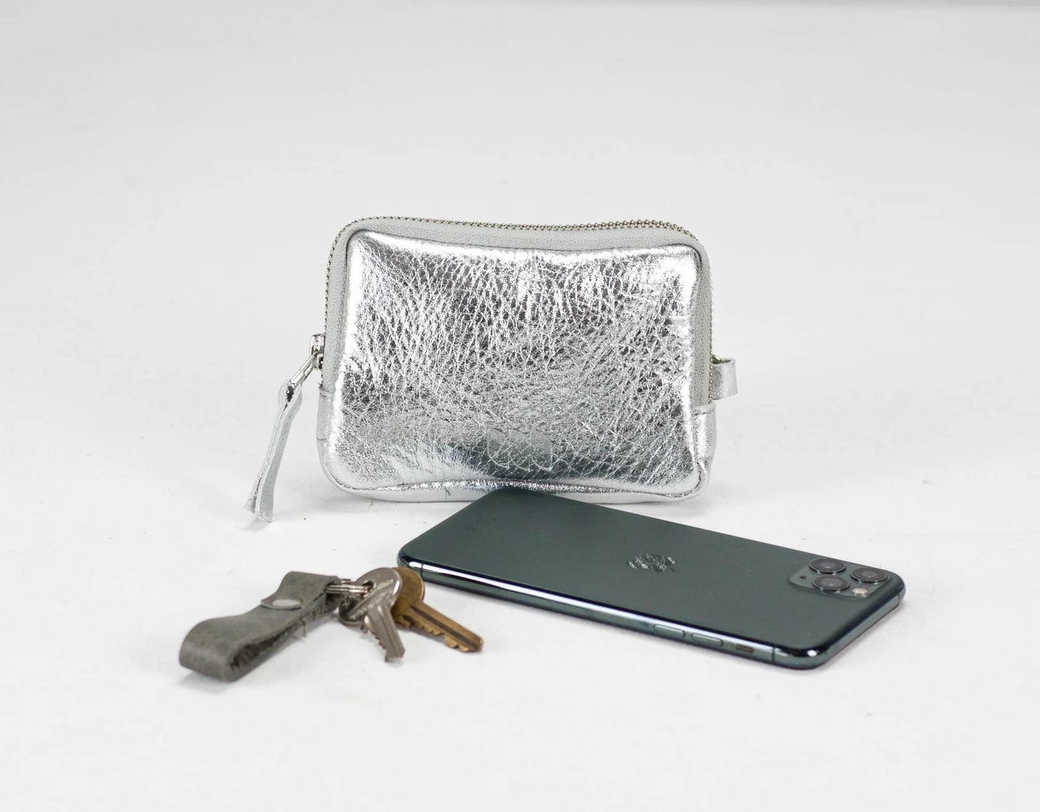 Silver metallic pouch, phone, and keys on a light gray background