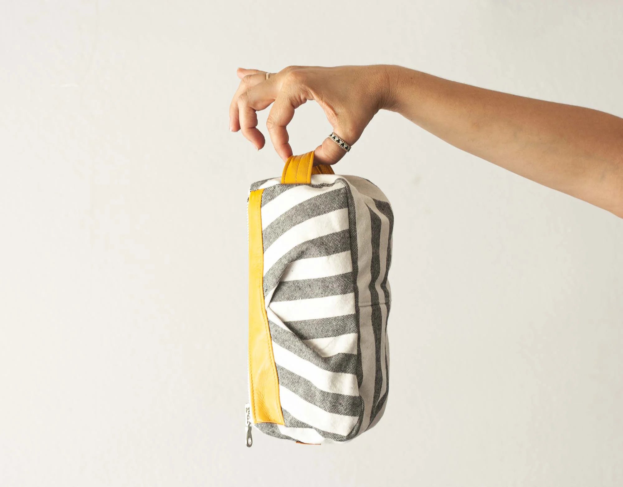 Hand holding a striped pouch with a yellow pull tab against a light background