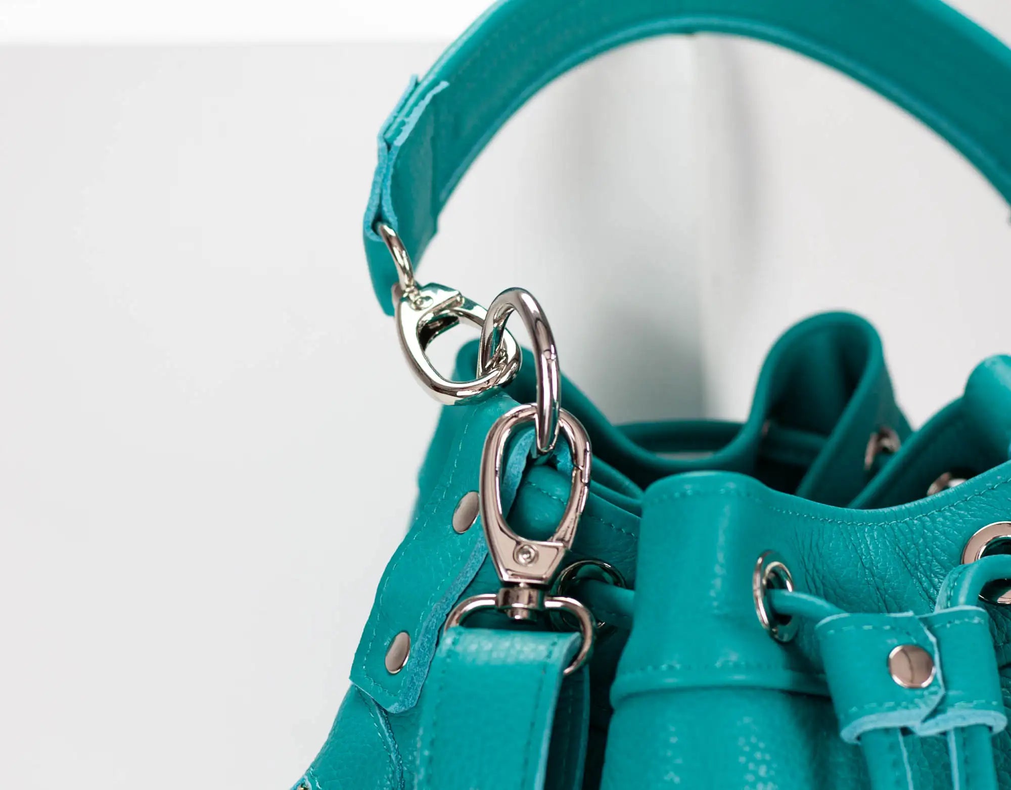 Close-up of a teal handbag with a silver clasp on a white background