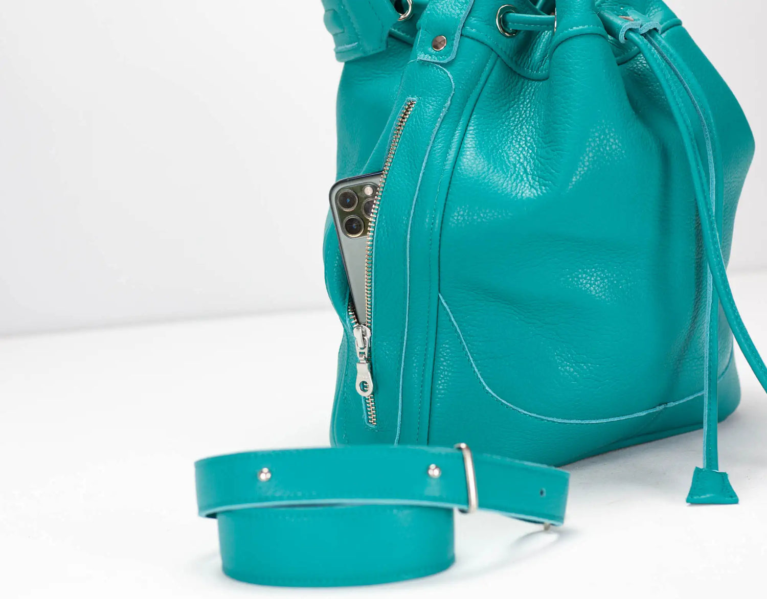 Turquoise leather bucket bag with a strap on a white background