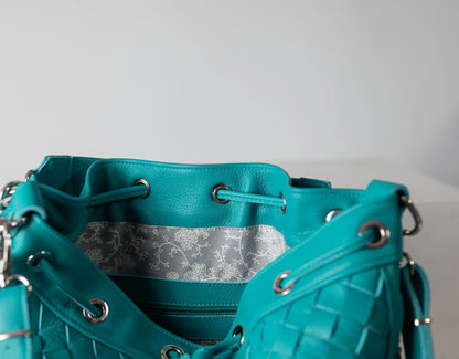 Teal handbag with textured surface and floral patterned interior on a light gray background