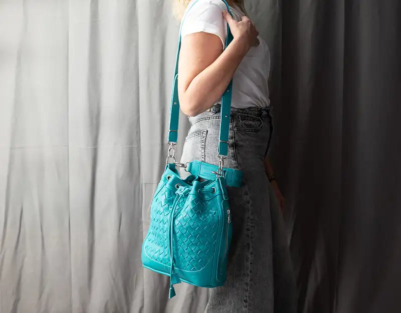Person wearing a turquoise quilted bag with suspenders against a plain background