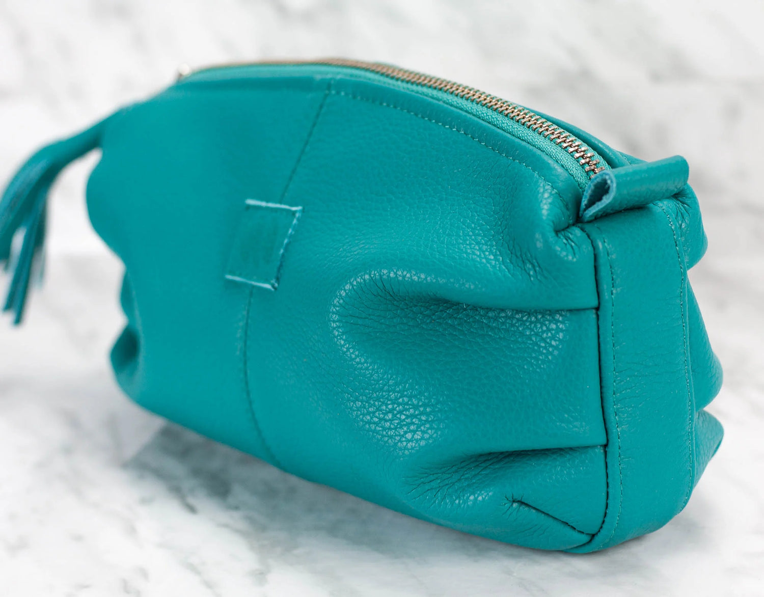 Teal leather clutch bag on a light gray background