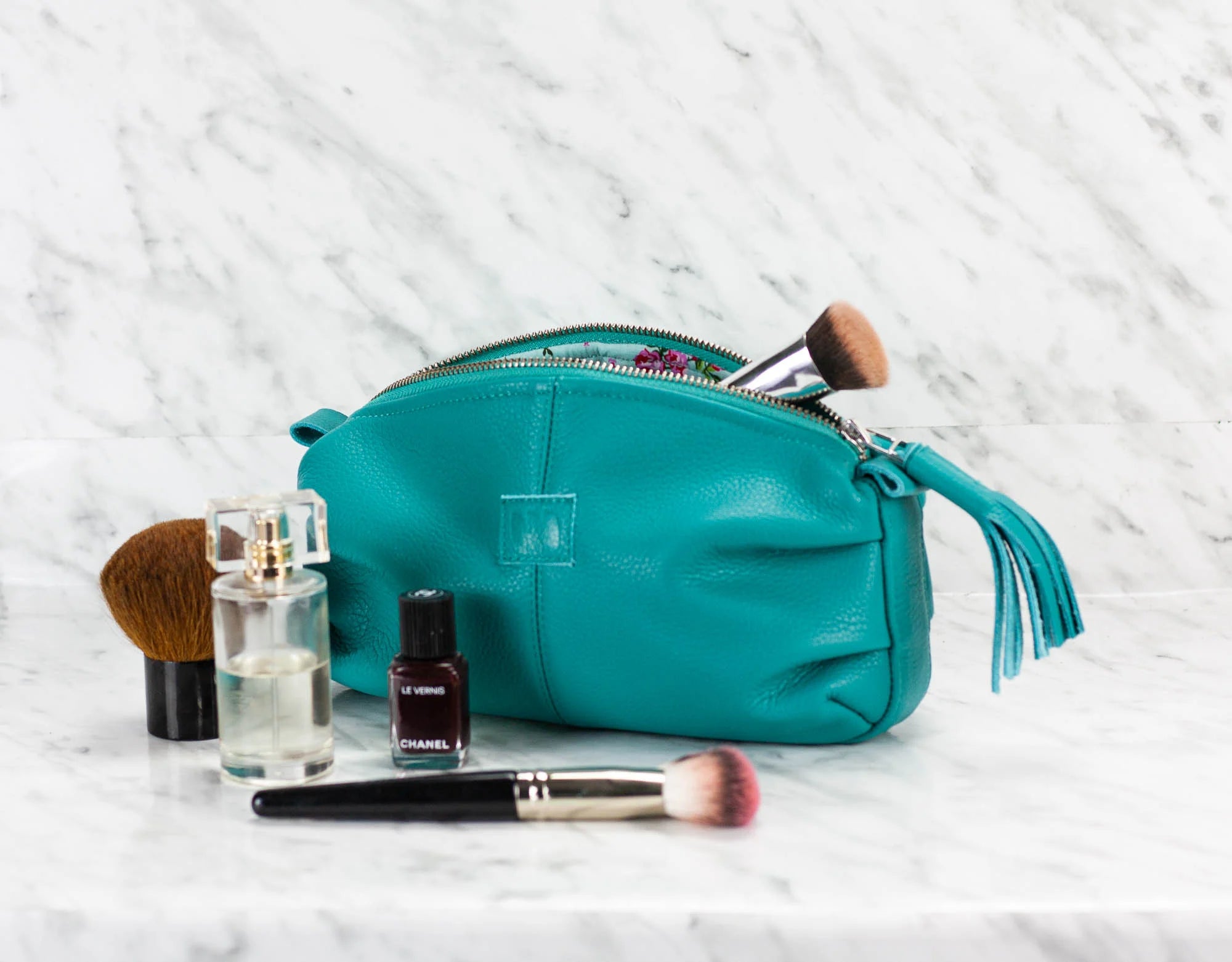 Teal makeup bag with cosmetic items on a marble surface