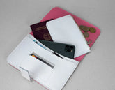 White wallet with pink interior, containing a phone, passport, and coins on a gray background