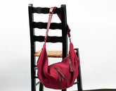 Red handbag with a strap on a black wooden chair against a white background