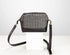 A small crossbody bag with a black leather base and trim, featuring a woven tweed pattern front panel in black, white, and gray. It has a long black leather shoulder strap and is displayed on a white block against a light gray background.