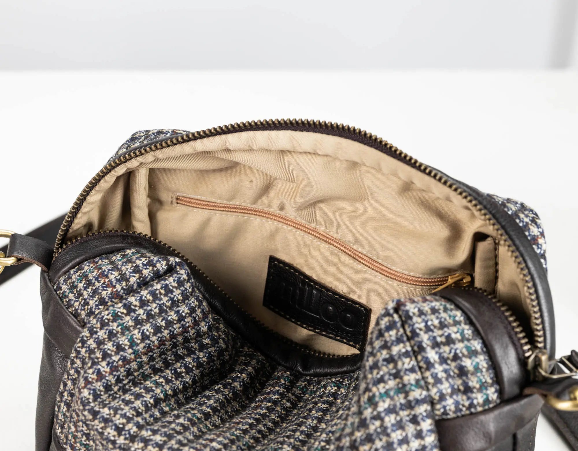 Close-up of an open handbag showing the interior lining, zipper, and a multicolor houndstooth patterned fabric exterior with dark brown leather trim.