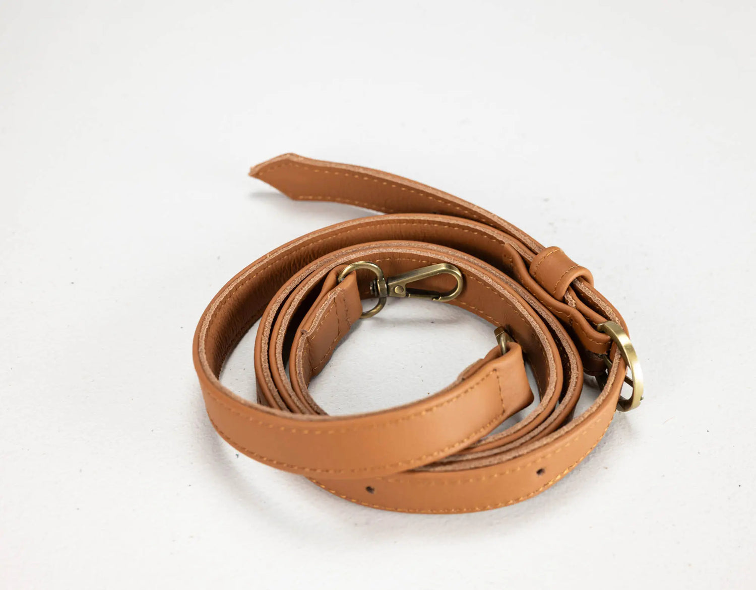 A tan faux-leather shoulder strap with brass-colored metal hardware, coiled on a plain white background.