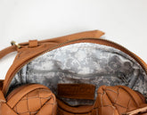 Close-up of a brown woven leather bag interior with a gray floral-patterned lining and a small brown brand patch reading &