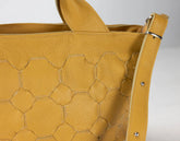 Close-up of a mustard yellow textured handbag with a strap on a light gray background