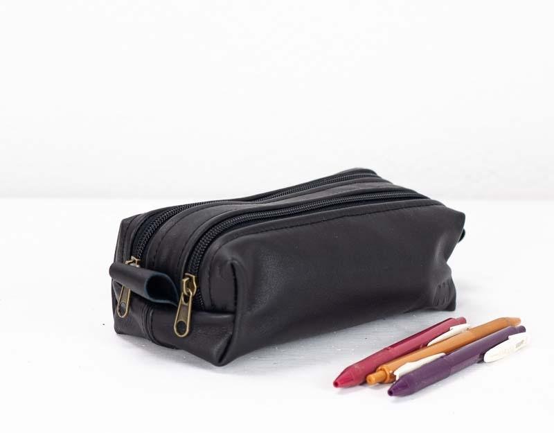 Black leather pencil case with a zipper compartment containing several pens, placed on a white background.